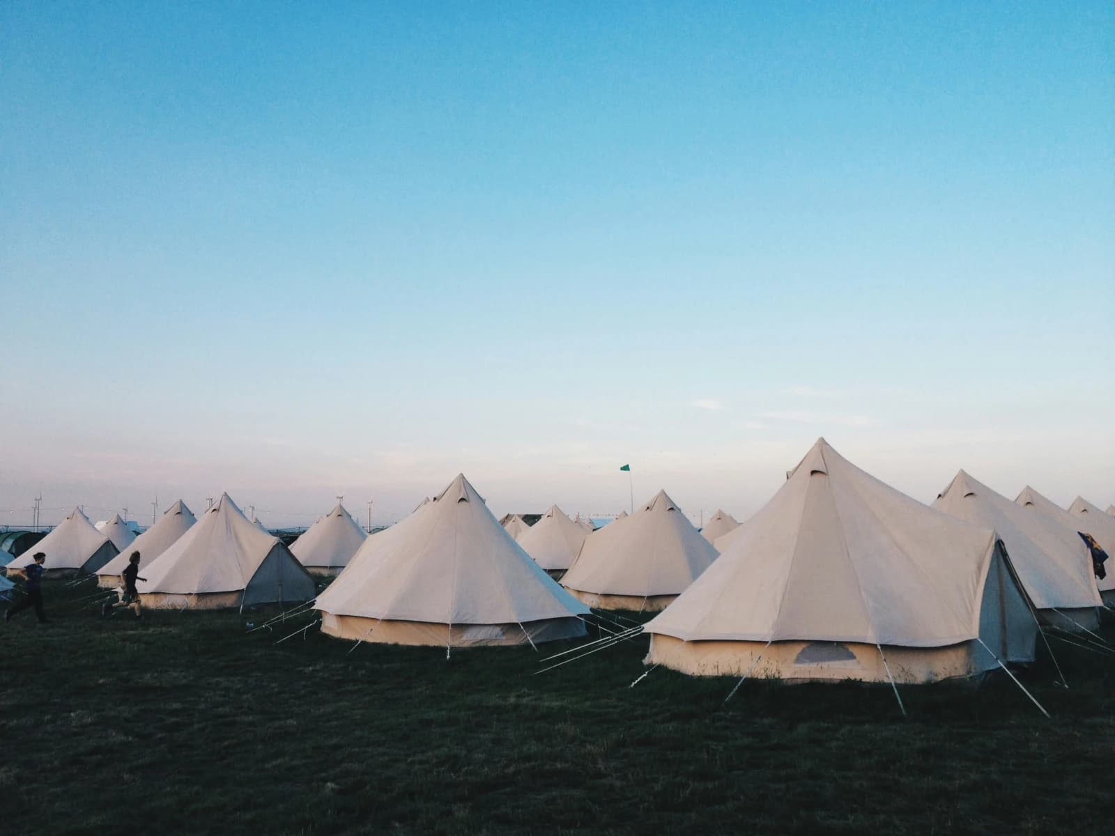 Rows of canvas bell tents pitched across a field at dusk