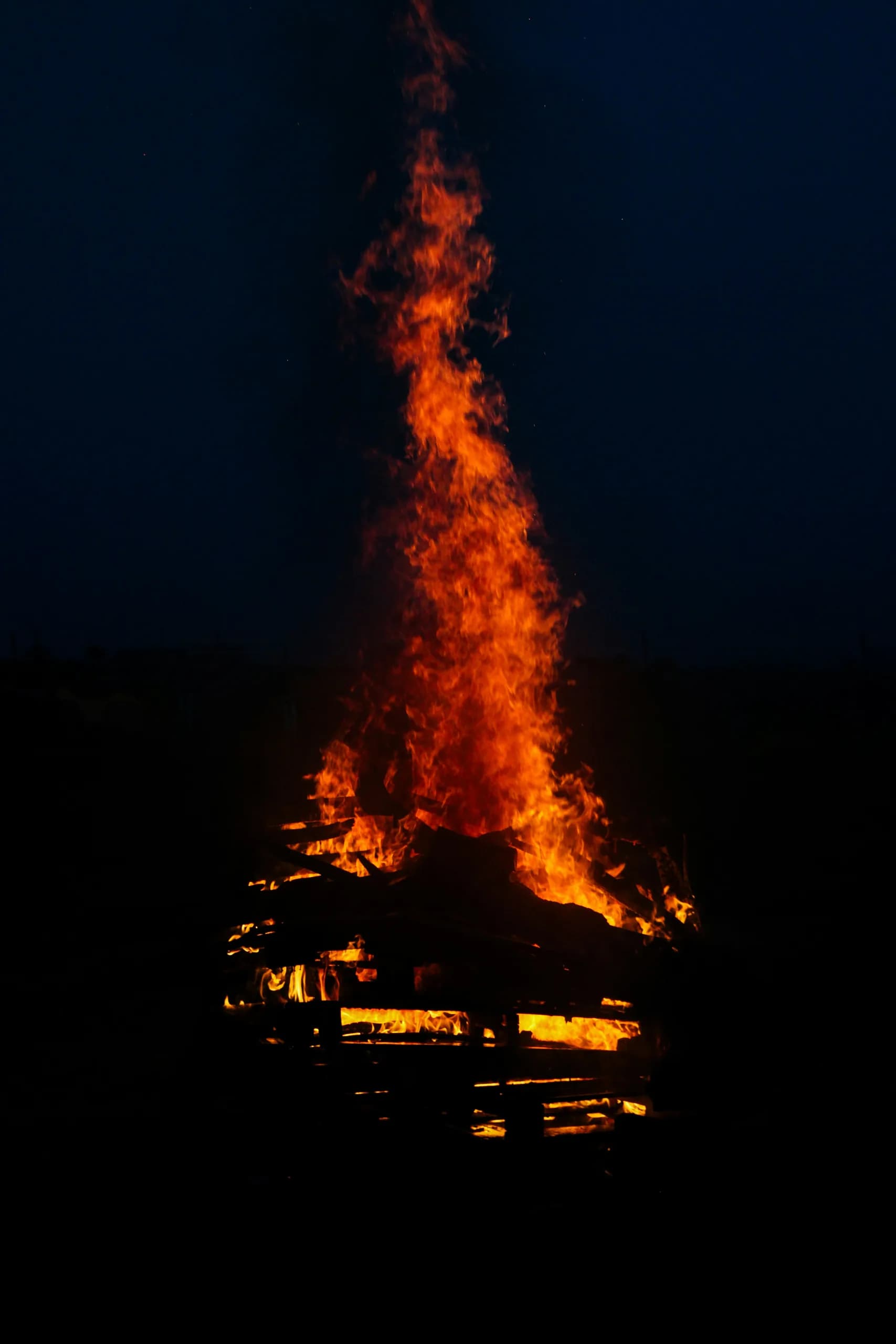 A towering festival bonfire at night